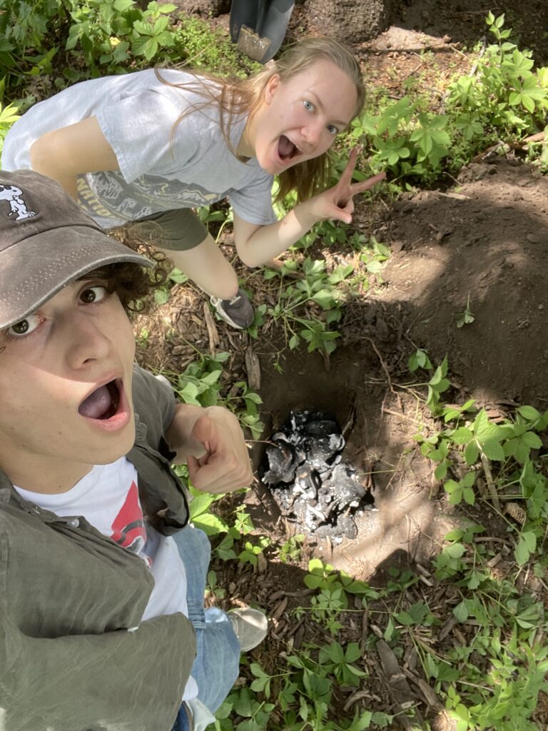 A picture of Martin Barroso and Elinor Fischer standing over a pit filled with charred bones